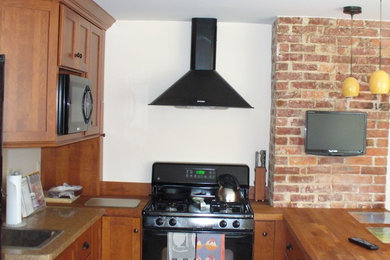 ボストンにある中くらいなトランジショナルスタイルのおしゃれなキッチン (ドロップインシンク、落し込みパネル扉のキャビネット、中間色木目調キャビネット、木材カウンター、黒い調理設備、コルクフローリング) の写真