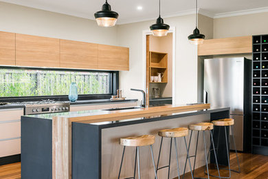 Inredning av ett modernt mellanstort kök, med en integrerad diskho, luckor med upphöjd panel, skåp i ljust trä, bänkskiva i kvarts, fönster som stänkskydd, rostfria vitvaror, mellanmörkt trägolv, en köksö och brunt golv