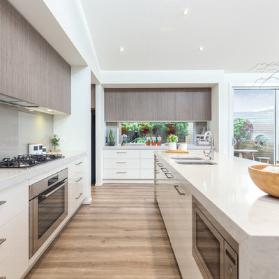 Inspiration for a contemporary galley light wood floor open concept kitchen remodel in Adelaide with a double-bowl sink, flat-panel cabinets, white cabinets, marble countertops, gray backsplash, glass sheet backsplash, stainless steel appliances and an island