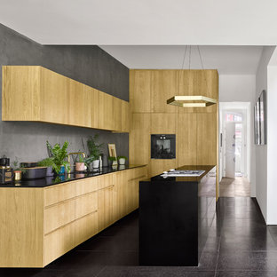 Inspiration for a contemporary l-shaped kitchen in London with an integrated sink, flat-panel cabinets, light wood cabinets, grey splashback, an island, black floors and black worktops.