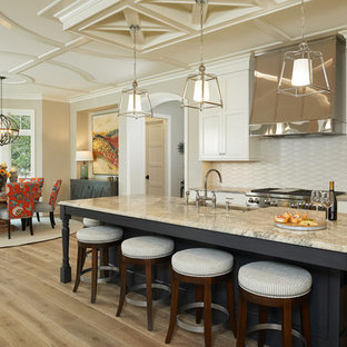 Photo of a beach style eat-in kitchen in Grand Rapids with recessed-panel cabinets, beige cabinets, beige splashback, stainless steel appliances, light hardwood floors, with island and quartzite benchtops.
