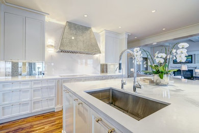 Example of a large transitional l-shaped medium tone wood floor eat-in kitchen design in Calgary with a double-bowl sink, recessed-panel cabinets, white cabinets, quartz countertops, white backsplash, paneled appliances and an island