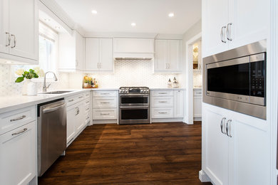 Large transitional u-shaped dark wood floor and brown floor eat-in kitchen photo in Toronto with an undermount sink, white cabinets, white backsplash, stainless steel appliances, white countertops, recessed-panel cabinets, quartz countertops, ceramic backsplash and an island