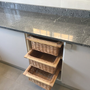Design ideas for a small modern l-shaped separate kitchen in Other with a double-bowl sink, flat-panel cabinets, grey cabinets, granite benchtops, black splashback, black appliances, terra-cotta floors, no island, beige floor, black benchtop and recessed.