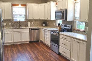 Mid-sized u-shaped laminate floor and brown floor eat-in kitchen photo in Other with a drop-in sink, shaker cabinets, white cabinets, laminate countertops, gray backsplash, ceramic backsplash, stainless steel appliances, no island and beige countertops