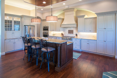 Example of a mid-sized classic l-shaped medium tone wood floor eat-in kitchen design in Orlando with an undermount sink, raised-panel cabinets, beige cabinets, granite countertops, beige backsplash, ceramic backsplash, stainless steel appliances and an island