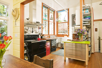 Small 1950s single-wall light wood floor and beige floor eat-in kitchen photo in San Francisco with a farmhouse sink, black appliances, an island and solid surface countertops