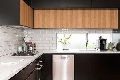 Modern inredning av ett mellanstort vit vitt kök, med en enkel diskho, släta luckor, svarta skåp, marmorbänkskiva, fönster som stänkskydd, rostfria vitvaror, mellanmörkt trägolv, vitt stänkskydd och brunt golv