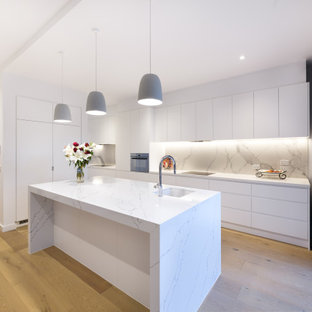 Large contemporary l-shaped kitchen in Melbourne with an undermount sink, flat-panel cabinets, white cabinets, grey splashback, panelled appliances, with island, beige floor and white benchtop.