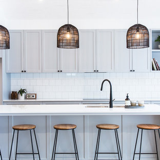 Foto di una grande cucina minimalista con lavello sottopiano, ante in stile shaker, ante grigie, top in quarzo composito, paraspruzzi bianco, paraspruzzi con piastrelle in ceramica, elettrodomestici neri, pavimento in legno massello medio, isola, pavimento marrone e top bianco