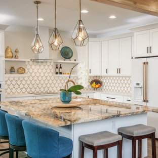 This is an example of a mid-sized transitional l-shaped open plan kitchen in Seattle with an undermount sink, shaker cabinets, white cabinets, granite benchtops, multi-coloured splashback, porcelain splashback, white appliances, vinyl floors, with island, brown floor and beige benchtop.