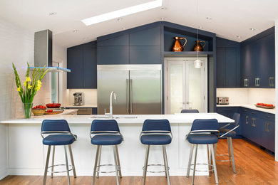 Large trendy u-shaped medium tone wood floor, orange floor and vaulted ceiling open concept kitchen photo in Other with an undermount sink, flat-panel cabinets, blue cabinets, quartz countertops, white backsplash, ceramic backsplash, stainless steel appliances, an island and white countertops