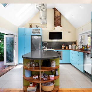 Contemporary l-shaped kitchen in Melbourne with flat-panel cabinets, blue cabinets, wood benchtops, black splashback, stainless steel appliances, with island, grey floor, brown benchtop and vaulted.
