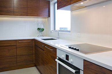 Bild på ett avskilt funkis u-kök, med en undermonterad diskho, släta luckor, skåp i mörkt trä, bänkskiva i kvarts, vitt stänkskydd, glaspanel som stänkskydd och vita vitvaror