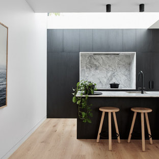 Mid-sized contemporary galley kitchen in Sydney with an integrated sink, flat-panel cabinets, black cabinets, grey splashback, panelled appliances, light hardwood floors, a peninsula, beige floor and grey benchtop.