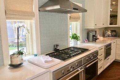 Kitchen - large traditional medium tone wood floor kitchen idea in Houston with an undermount sink, shaker cabinets, white cabinets, solid surface countertops, blue backsplash, glass tile backsplash, stainless steel appliances and an island