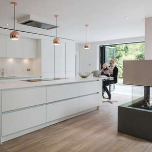 Modern kitchen in West Midlands with a submerged sink, flat-panel cabinets, white cabinets, white splashback, light hardwood flooring, an island, beige floors and white worktops.