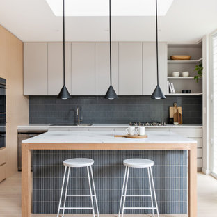Contemporary u-shaped kitchen in Sydney with a drop-in sink, flat-panel cabinets, white cabinets, grey splashback, panelled appliances, light hardwood floors, beige floor and white benchtop.