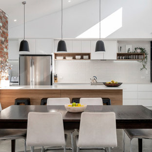 Design ideas for a mid-sized industrial galley open plan kitchen in Perth with concrete floors, flat-panel cabinets, white cabinets, white splashback, subway tile splashback, a peninsula, grey floor and white benchtop.