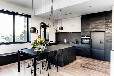 Inspiration for a large scandinavian l-shaped light wood floor open concept kitchen remodel in Perth with black backsplash, an island, flat-panel cabinets, black appliances, a drop-in sink and black cabinets