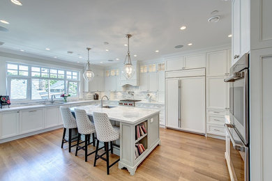 Large transitional l-shaped light wood floor and brown floor kitchen photo in Vancouver with an undermount sink, shaker cabinets, white cabinets, marble countertops, gray backsplash and an island