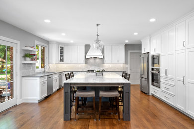 Example of a large transitional l-shaped medium tone wood floor and brown floor open concept kitchen design in St Louis with an undermount sink, recessed-panel cabinets, white cabinets, quartz countertops, gray backsplash, stone tile backsplash, stainless steel appliances, an island and gray countertops