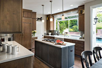 Inspiration for a mid-sized transitional u-shaped medium tone wood floor and brown floor kitchen remodel in Orange County with a farmhouse sink, medium tone wood cabinets, quartz countertops, gray backsplash, glass tile backsplash, paneled appliances and white countertops