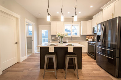 Large classic l-shaped enclosed kitchen in Calgary with shaker cabinets, white cabinets, an island, marble worktops, grey splashback, white worktops, a submerged sink, metro tiled splashback, black appliances, medium hardwood flooring and brown floors.