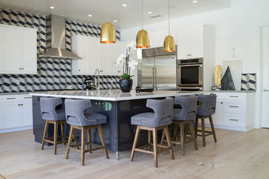 Example of a transitional l-shaped light wood floor and beige floor kitchen design in Orange County with a farmhouse sink, white cabinets, quartzite countertops, ceramic backsplash, stainless steel appliances, shaker cabinets, gray backsplash and an island
