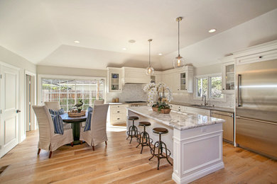 Example of a classic light wood floor eat-in kitchen design in Orange County with an undermount sink, raised-panel cabinets, white cabinets, marble countertops, stainless steel appliances and an island