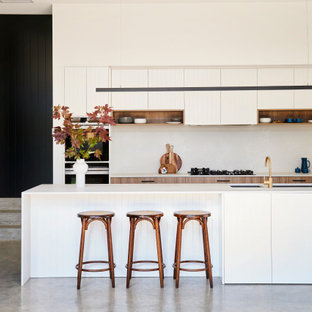 Photo of a large contemporary l-shaped kitchen in Geelong with an undermount sink, flat-panel cabinets, white cabinets, black appliances, with island, grey floor, white benchtop, white splashback and concrete floors.