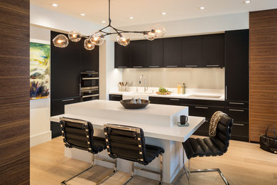 Example of a mid-sized trendy l-shaped light wood floor eat-in kitchen design in San Francisco with a farmhouse sink, recessed-panel cabinets, black cabinets, quartz countertops, gray backsplash, paneled appliances and an island