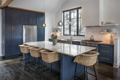 Example of a mountain style dark wood floor kitchen design in Other with a farmhouse sink, shaker cabinets, blue cabinets, white backsplash, stainless steel appliances and an island