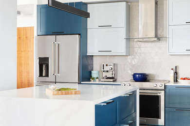 Mittelgroße Moderne Wohnküche in L-Form mit Waschbecken, Schrankfronten im Shaker-Stil, blauen Schränken, Quarzwerkstein-Arbeitsplatte, Küchenrückwand in Beige, Rückwand aus Keramikfliesen, Küchengeräten aus Edelstahl, dunklem Holzboden, Kücheninsel, braunem Boden und weißer Arbeitsplatte in Toronto