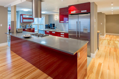 Photo of a medium sized modern galley open plan kitchen in Vancouver with flat-panel cabinets, red cabinets, engineered stone countertops, stainless steel appliances, porcelain flooring, an island, a double-bowl sink, beige splashback, glass tiled splashback and grey floors.