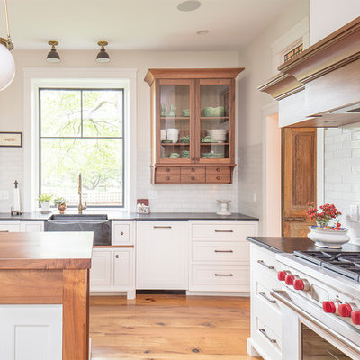 Kitchen - mid-sized farmhouse l-shaped medium tone wood floor and brown floor kitchen idea in Philadelphia with a farmhouse sink, shaker cabinets, white cabinets, soapstone countertops, white backsplash, brick backsplash, paneled appliances, an island and black countertops