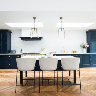 Photo of an expansive traditional galley kitchen/diner in London with a built-in sink, blue cabinets, marble worktops, white splashback, marble splashback, white appliances, white worktops, shaker cabinets, medium hardwood flooring, an island and beige floors.