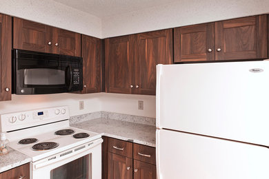 Klassisk inredning av ett litet grå grått kök, med en undermonterad diskho, skåp i shakerstil, skåp i mellenmörkt trä, granitbänkskiva, vita vitvaror och ljust trägolv