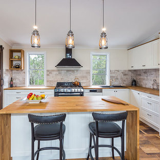 Small traditional l-shaped open plan kitchen in Brisbane with a double-bowl sink, recessed-panel cabinets, white cabinets, wood benchtops, brown splashback, black appliances, medium hardwood floors, a peninsula and brown floor.