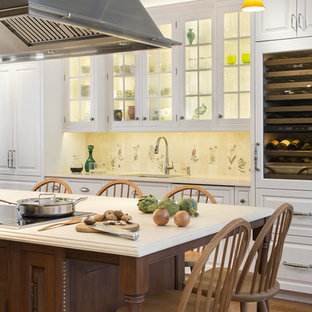 Imagen de cocina de galera, tradicional, grande, con armarios con paneles con relieve, puertas de armario blancas, salpicadero multicolor, electrodomésticos de acero inoxidable, suelo de madera en tonos medios, una isla, suelo marrón, encimera de piedra caliza, salpicadero de azulejos de porcelana, fregadero bajoencimera y encimeras beige