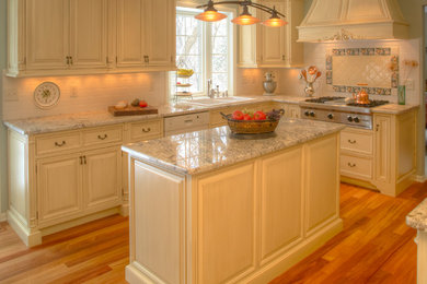 Example of a classic l-shaped eat-in kitchen design in Milwaukee with a double-bowl sink, raised-panel cabinets, yellow cabinets, white backsplash, ceramic backsplash and paneled appliances