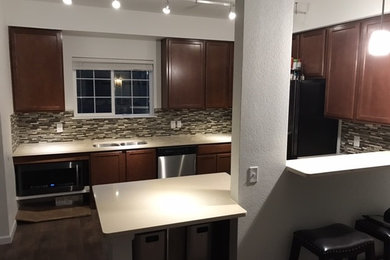 Medium sized traditional u-shaped kitchen/diner in Denver with a submerged sink, recessed-panel cabinets, dark wood cabinets, engineered stone countertops, multi-coloured splashback, glass tiled splashback, black appliances, dark hardwood flooring, a breakfast bar and brown floors.