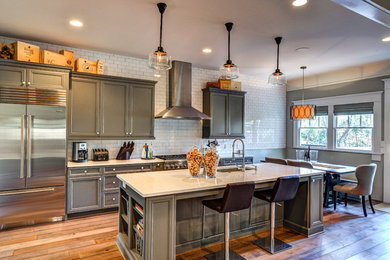Example of a large transitional galley medium tone wood floor open concept kitchen design in Atlanta with an undermount sink, beaded inset cabinets, gray cabinets, quartz countertops, white backsplash, ceramic backsplash, stainless steel appliances and an island