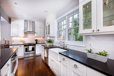 Example of a mid-sized transitional galley medium tone wood floor eat-in kitchen design in Atlanta with a farmhouse sink, flat-panel cabinets, white cabinets, granite countertops, white backsplash, subway tile backsplash, stainless steel appliances and a peninsula