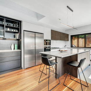 Large contemporary l-shaped eat-in kitchen in Sydney with a double-bowl sink, flat-panel cabinets, white cabinets, marble benchtops, white splashback, glass sheet splashback, stainless steel appliances, medium hardwood floors, with island, brown floor and grey benchtop.