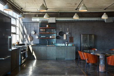 Inspiration för ett mellanstort industriellt svart svart kök, med släta luckor, grå skåp, granitbänkskiva, grått stänkskydd, betonggolv, en undermonterad diskho, rostfria vitvaror och brunt golv