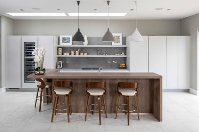 Photo of a large contemporary galley kitchen/diner in Dublin with a submerged sink, flat-panel cabinets, grey cabinets, engineered stone countertops, grey splashback, ceramic splashback, black appliances, ceramic flooring, an island, grey floors and grey worktops.