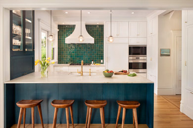 Example of a large 1950s single-wall medium tone wood floor and brown floor eat-in kitchen design with an undermount sink, shaker cabinets, white cabinets, marble countertops, green backsplash, ceramic backsplash, stainless steel appliances and an island