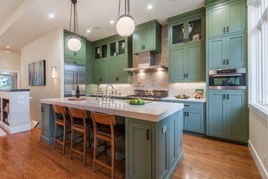 Inspiration for a mid-sized transitional l-shaped medium tone wood floor open concept kitchen remodel in San Francisco with a farmhouse sink, recessed-panel cabinets, green cabinets, quartz countertops, beige backsplash, ceramic backsplash, stainless steel appliances and an island