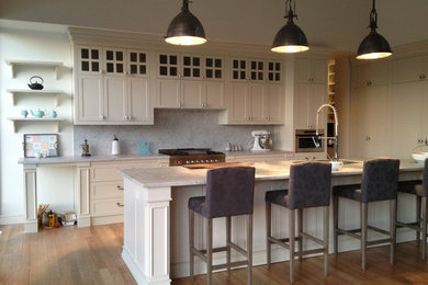 Idéer för ett mellanstort klassiskt vit linjärt kök med öppen planlösning, med en nedsänkt diskho, luckor med infälld panel, vita skåp, bänkskiva i kvarts, grått stänkskydd, stänkskydd i marmor, rostfria vitvaror, mellanmörkt trägolv, en köksö och brunt golv